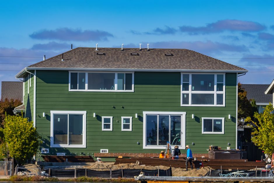 A modern green house under construction with blue skies and workers outside.